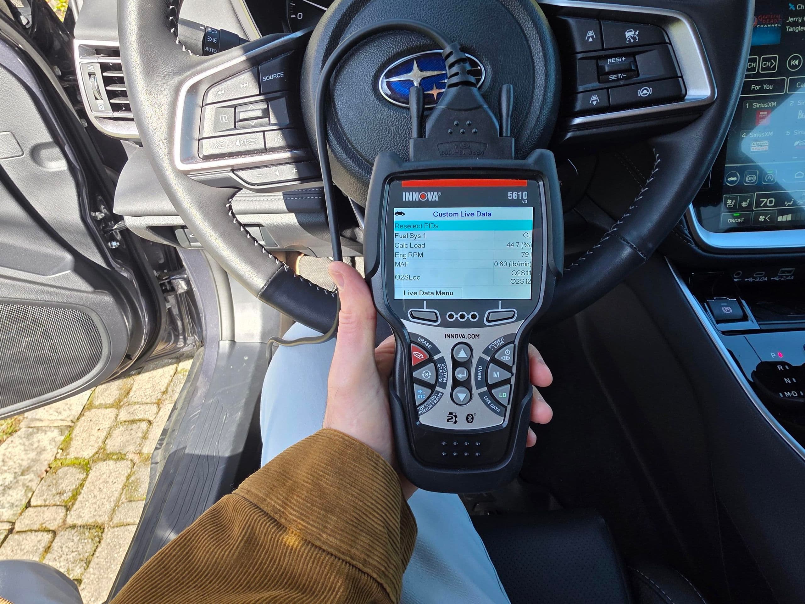 Hand holding an Innova 5610 diagnostic scanner displaying live engine data inside a Subaru.