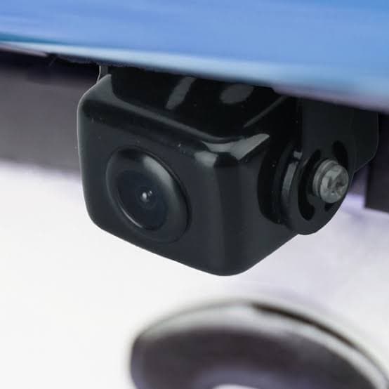A small black backup camera mounted underneath the rear bumper of a blue vehicle.