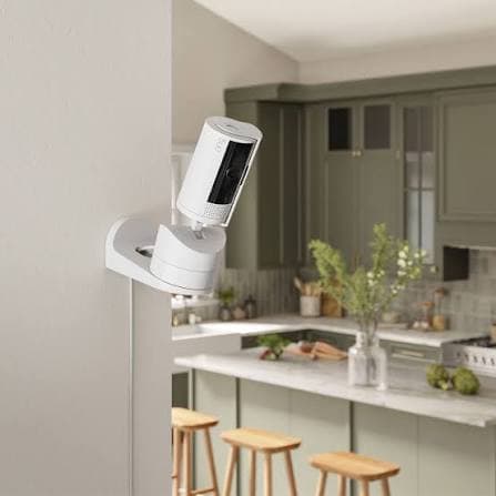 White Ring security camera mounted on a wall overlooking a modern kitchen with green cabinets.