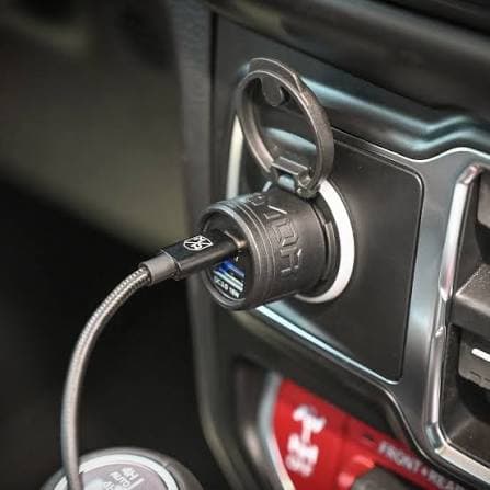 Black USB car charger plugged into a vehicle's dashboard outlet with a charging cable.